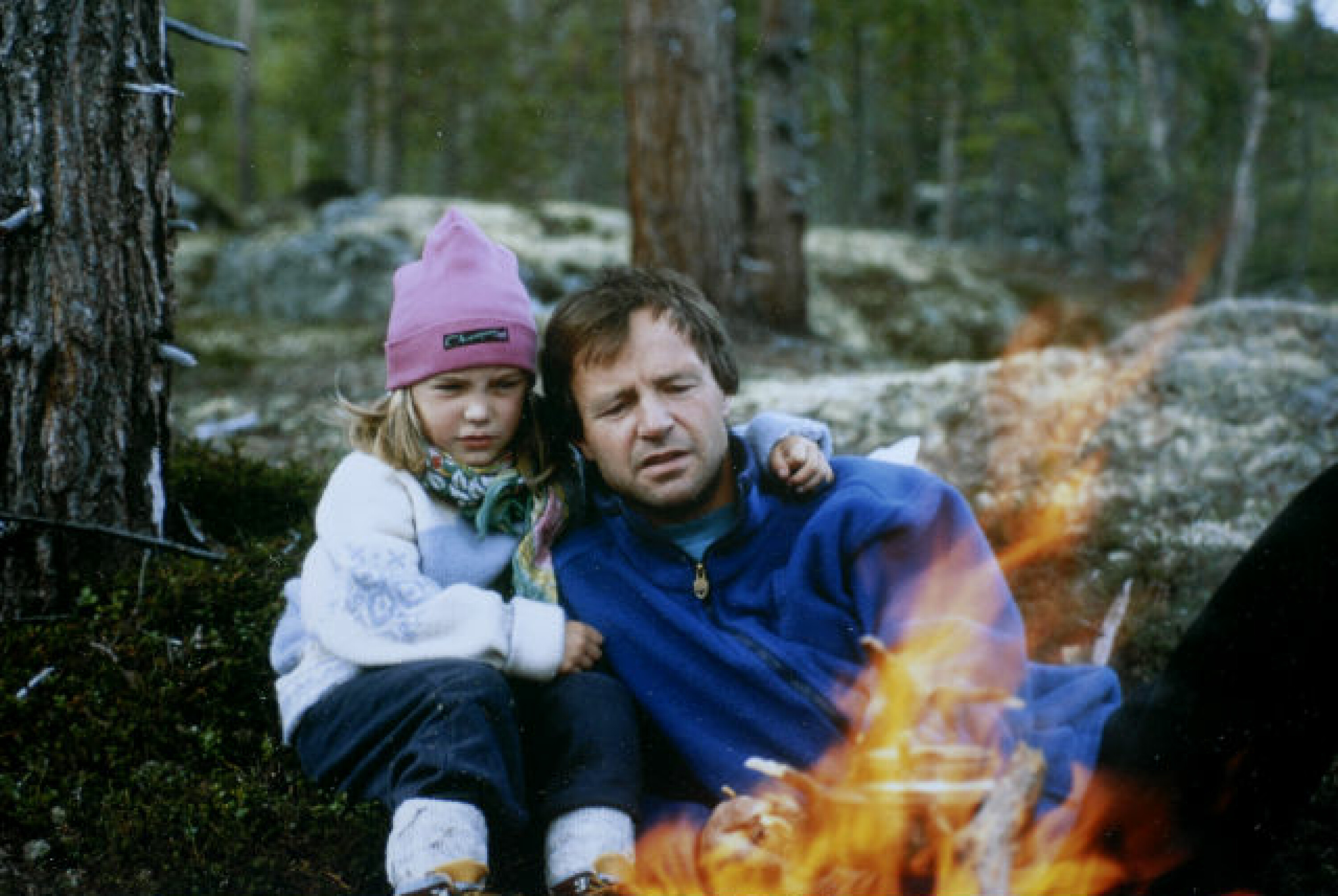 Mann og jente sitter ved et bål i skogen.